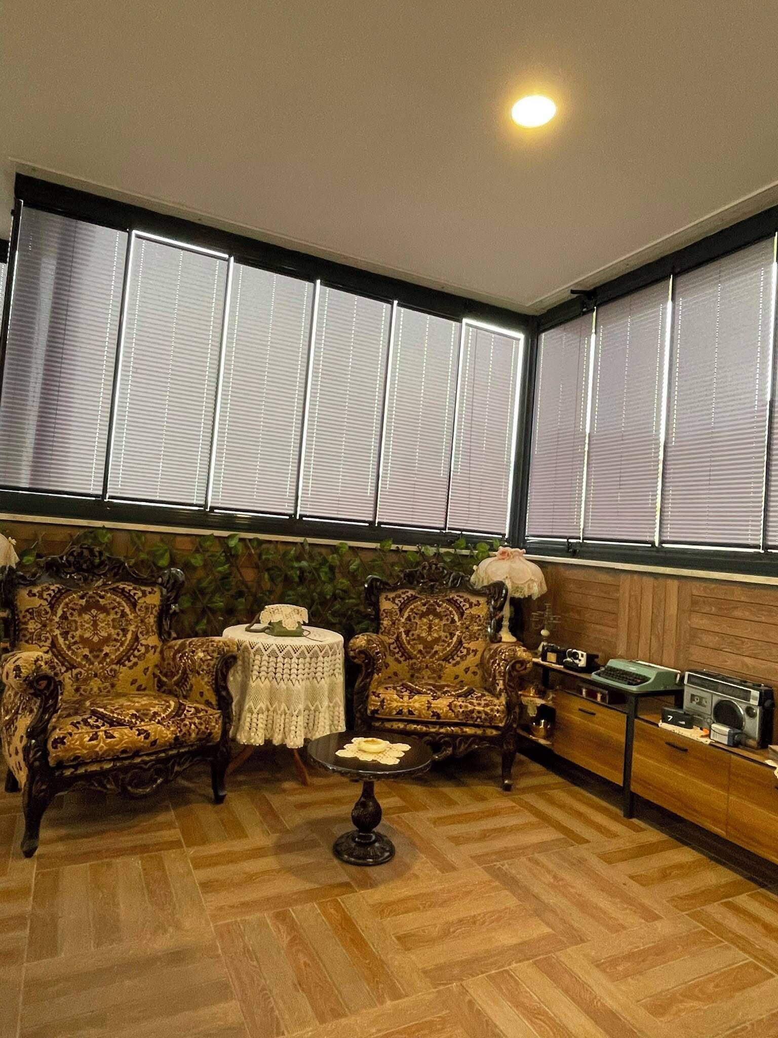 A room with two ornate armchairs, a small round table, and a cabinet with vintage radios.