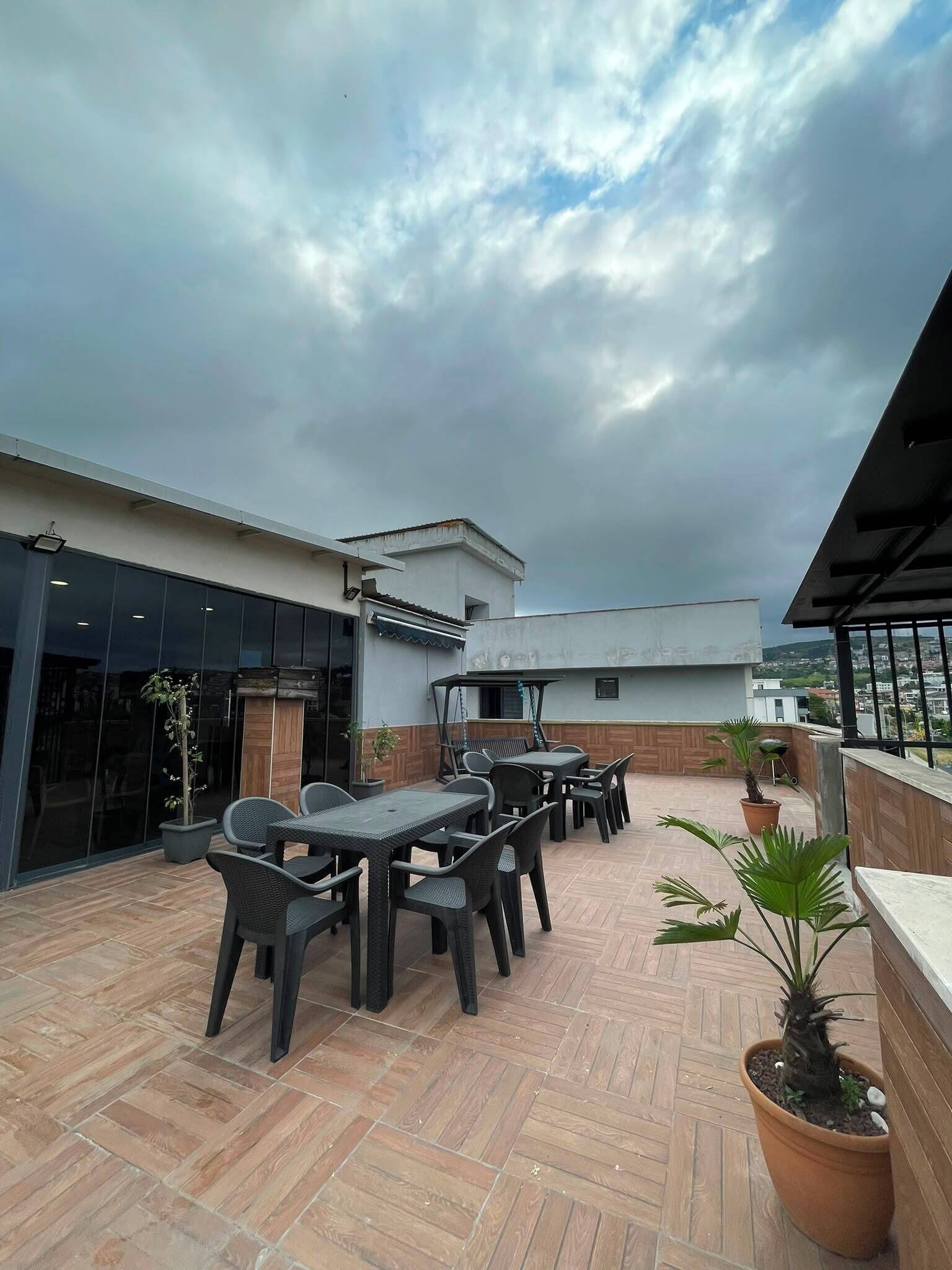 An outdoor patio area with tables and chairs, potted plants, and a view of the cityscape.