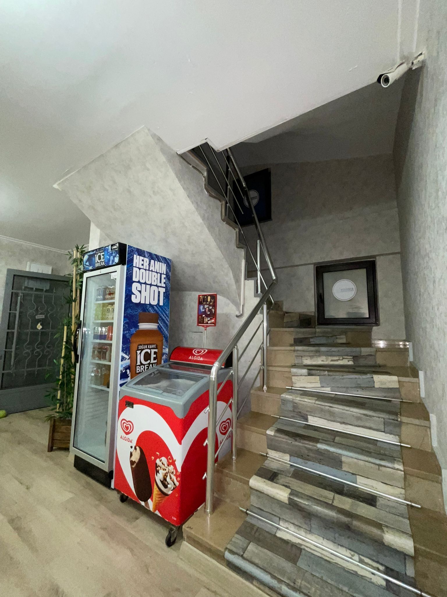 Un escalier au design évoquant la pierre, menant à un palier où se trouvent un tableau encadré et un distributeur automatique.