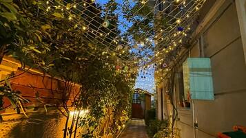 A narrow pathway with a tiled floor, surrounded by greenery and decorative lights.