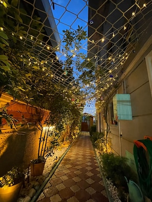 A narrow pathway with a tiled floor, surrounded by greenery and decorative lights. - Terrace Cordon Palace Hotel (Serdivan)
