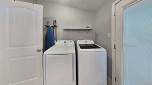 A laundry room with two white washing machines, a blue ironing board, and a shelf with cleaning supplies. - Al & Sherry's Oasis (Rockport)