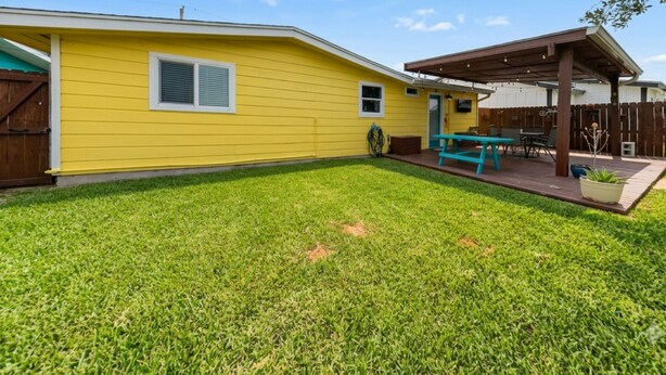 A residential backyard with a yellow house, a wooden deck, and a covered patio area. - Al & Sherry's Oasis (Rockport)