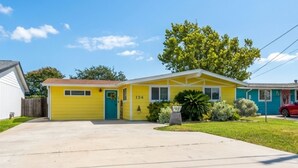 A single-story yellow house with a blue door, number 134, and a red car parked in the driveway. - Al & Sherry's Oasis (Rockport)