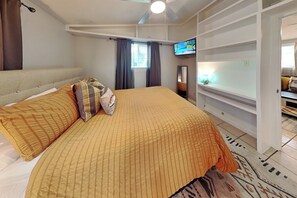 Ein Schlafzimmer mit einem Bett, einem Fernseher, einem Deckenventilator und einem Fenster mit Vorhängen.