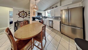 A modern kitchen with a stainless steel refrigerator, wooden dining table, and a ship's wheel decoration. - Al & Sherry's Oasis (Rockport)