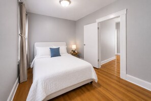 Ein Schlafzimmer mit Bett, Nachttisch, Lampe und einer Tür zu einem anderen Raum.