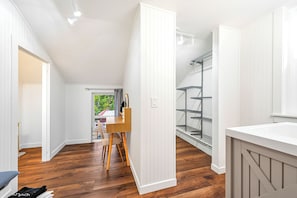 A room with a wooden floor, white walls, a desk with a chair, and a window with a view of greenery.