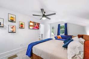 A bedroom with a bed, a sofa, a ceiling fan, and a TV.
