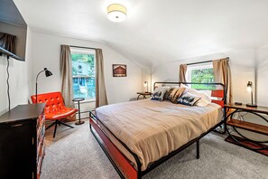 A bedroom with a bed, a desk, a chair, and a window with curtains.