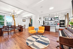 A spacious living room with a dining area, a kitchen, and a piano.