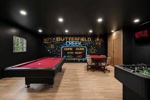 Ein Zimmer mit Billardtisch, Kicker und einem Neon-Schild mit der Aufschrift 'Butterfield Creek Game Over Stay Again?'