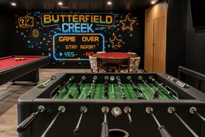 Een tafelvoetbaltafel, een pooltafel en een neonbord met de tekst 'BUTTERFIELD CREEK' en 'GAME OVER'.