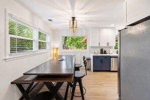 A modern kitchen with white cabinets, a stainless steel refrigerator, and a dining area with a wooden table and chairs. - Creek Retreat on 1 acre / Game Room / Fire Pit (Matteson)