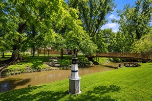 Ein Park mit einem Fluss, einer Holzbrücke und einem turmartigen Gebäude.