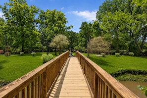 Een houten terras leidt naar een pergola in een weelderig groen park.