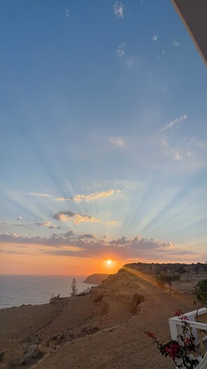 A coastal landscape with a sunset, rocky terrain, and a view of the sea. - Villa Mousouna - Panoramic Sea View of Lefkos (Kato Lefkos)