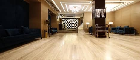 A spacious lobby with a wooden floor, a blue sofa, and a reception desk.