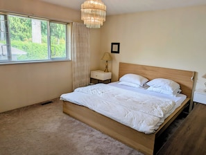 A bedroom with a wooden bed, a bedside table, a lamp, and a window with blinds.