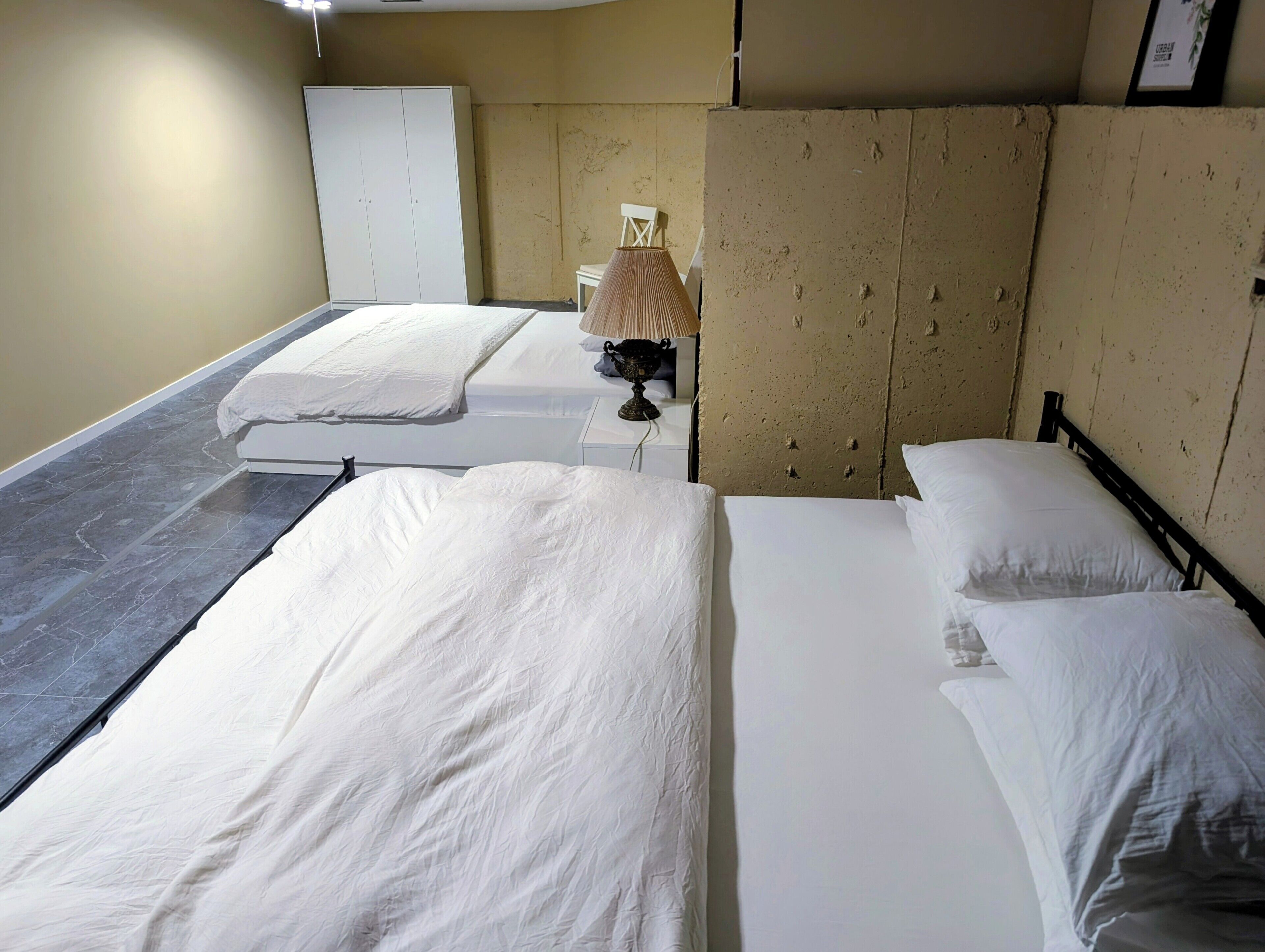 A hotel room with two beds, a bedside table, a lamp, and a wardrobe.