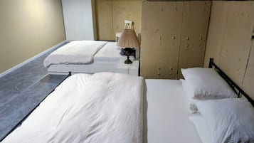 A hotel room with two beds, a bedside table, a lamp, and a wardrobe.