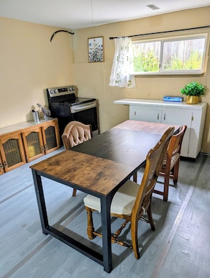 A dining area with a wooden table and chairs, a kitchen with a stove and oven, and a window with a curtain.