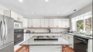 A modern kitchen with white cabinets, a stainless steel refrigerator, a built-in oven, a microwave, a gas stove, and a dishwasher.