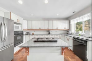 A modern kitchen with white cabinets, a stainless steel refrigerator, a built-in oven, a microwave, a gas stove, and a dishwasher.