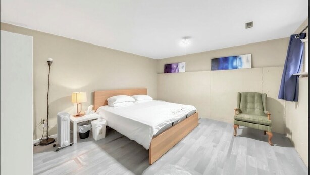 A bedroom with a bed, bedside table, lamp, chair, and artwork on the wall.