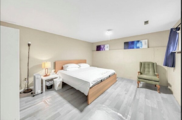 A bedroom with a bed, bedside table, lamp, chair, and artwork on the wall.