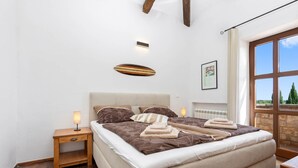 Een slaapkamer met een groot bed, nachtkastje, lamp, radiator en een raam met uitzicht.