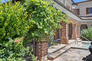 Ein Innenhof mit Backsteinmauer, einem Pool und einer mit Grünpflanzen bewachsenen Pergola.