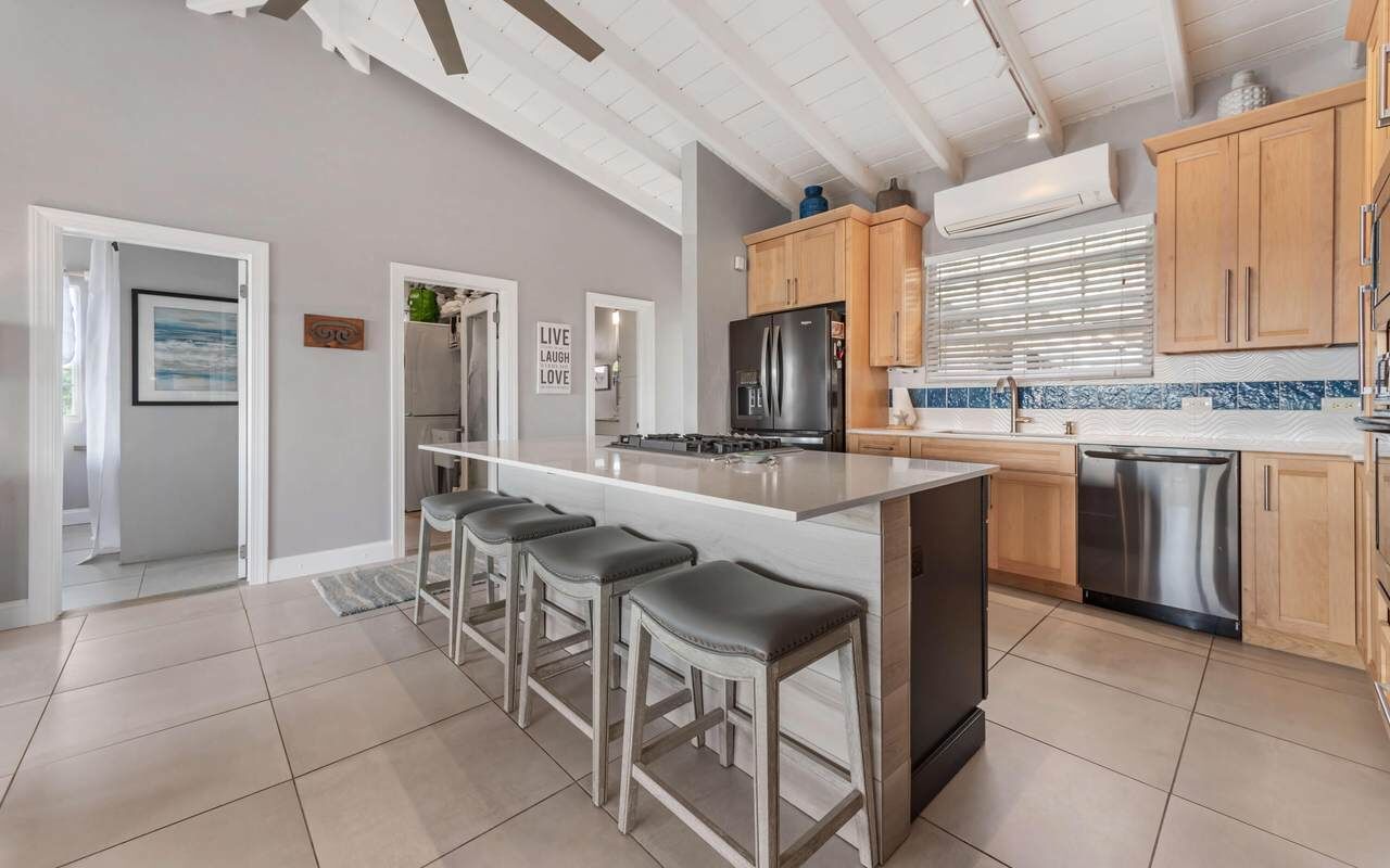 A modern kitchen with a central island, bar stools, wooden cabinets, and stainless steel appliances.