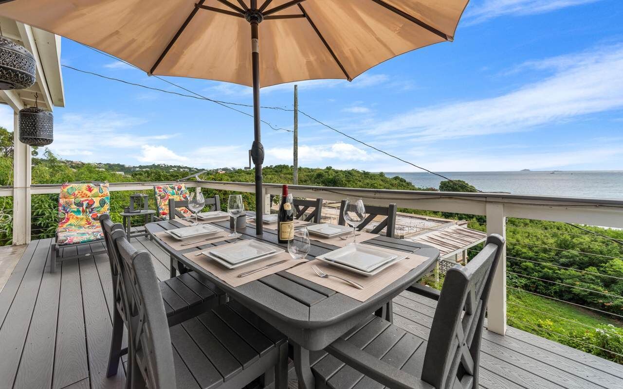 A deck with a table set for dining, overlooking a body of water.