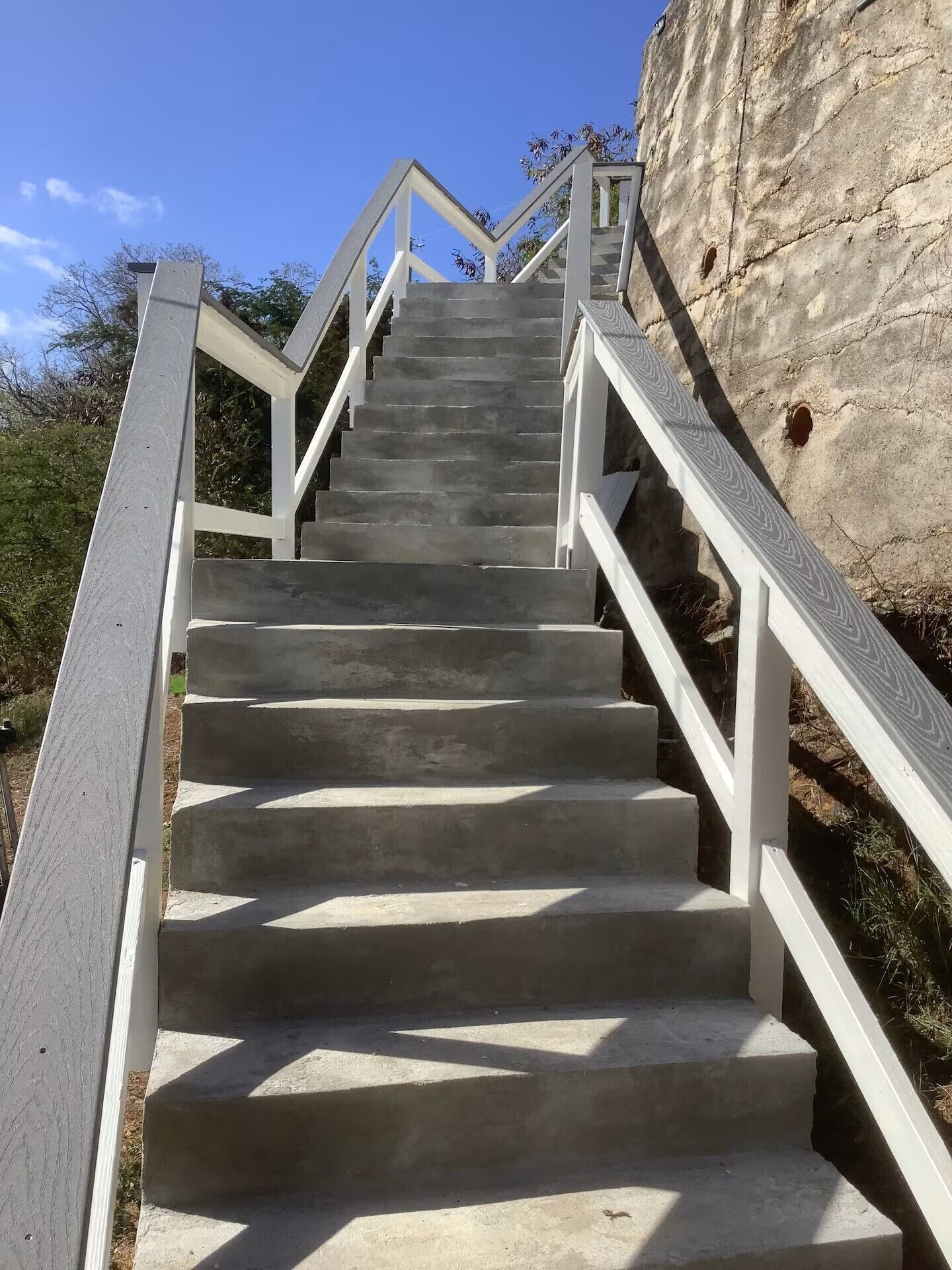 Un escalier en béton, agrémenté de rampes blanches, mène vers le haut d’une colline rocheuse.
