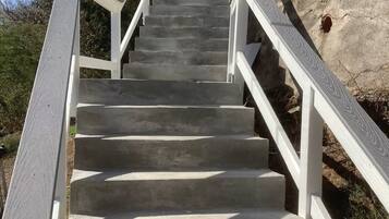 Un escalier en béton, agrémenté de rampes blanches, mène vers le haut d’une colline rocheuse.