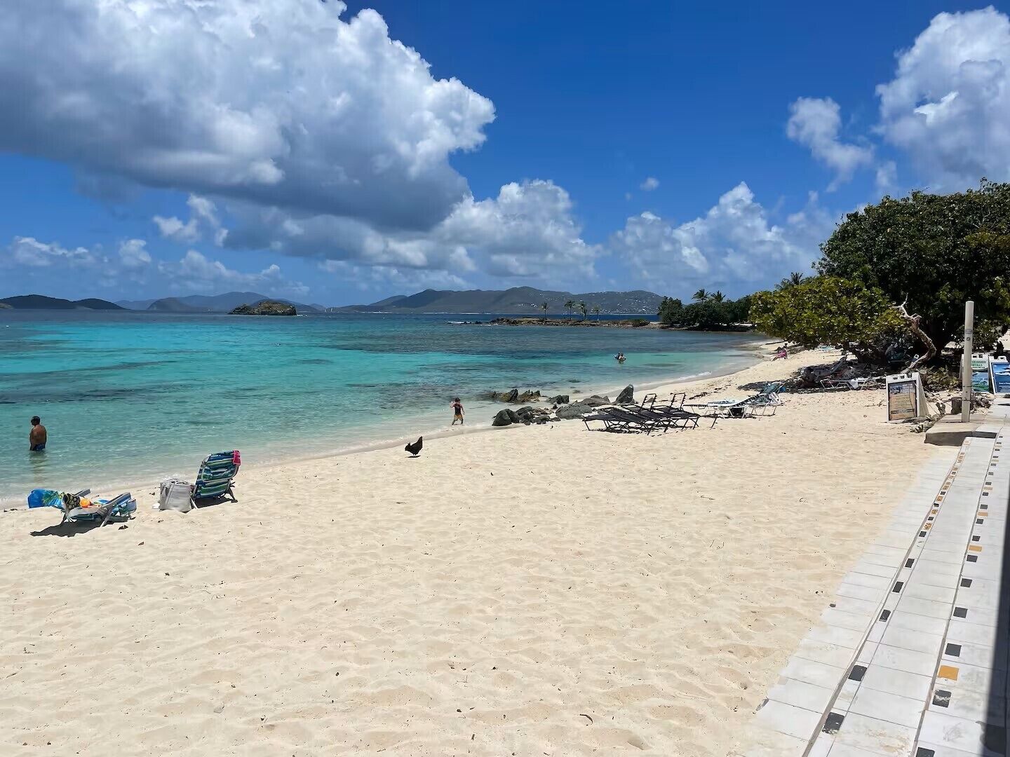 A beach with clear turquoise water, a sandy shore, and a few people and birds.