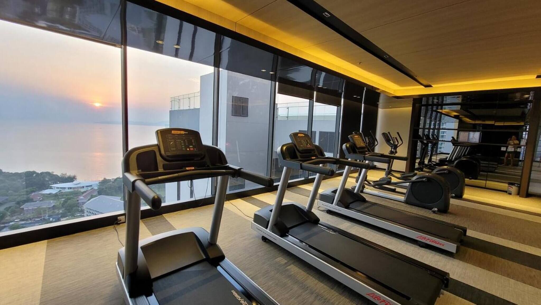 A gym with treadmills and exercise equipment, large windows with a city view, and a modern interior design.