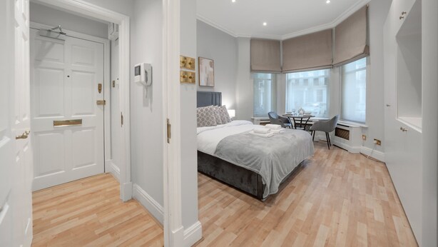 Een slaapkamer met een bed, nachtkastje, stoel en een raam met gordijnen.
