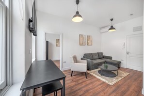 Ein modernes Wohnzimmer mit einer Couch, einem Sessel, einem Couchtisch und einem an der Wand befestigten Fernseher.