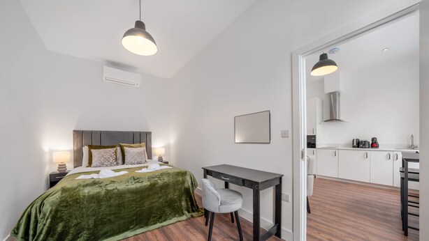 Ein Hotelzimmer mit einem Bett, einem Nachttisch und einem kleinen Schreibtisch mit Stuhl. Ein kleines Küchenzimmer ist anliegend.