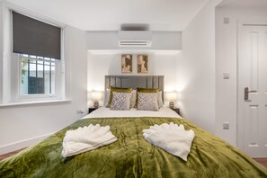 Ein Hotelzimmer mit einem Bett, zwei Nachttischlampen, einem Fenster mit Jalousie, einer Klimaanlage und einer Tür.