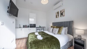 A modern hotel room with a bed, bedside table, and a kitchenette. - Bright Studio in Knightsbridge (London)