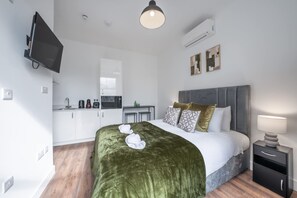 A modern hotel room with a bed, bedside table, and a kitchenette. - Bright Studio in Knightsbridge (London)