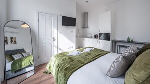 A bedroom with a bed, a mirror, a television, a kitchenette, and a door. - Bright Studio in Knightsbridge (London)