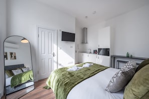 A bedroom with a bed, a mirror, a television, a kitchenette, and a door. - Bright Studio in Knightsbridge (London)