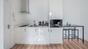 A compact kitchen with white cabinets, a stainless steel sink, and a black countertop. - Bright Studio in Knightsbridge (London)