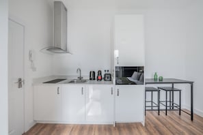 A compact kitchen with white cabinets, a stainless steel sink, and a black countertop. - Bright Studio in Knightsbridge (London)