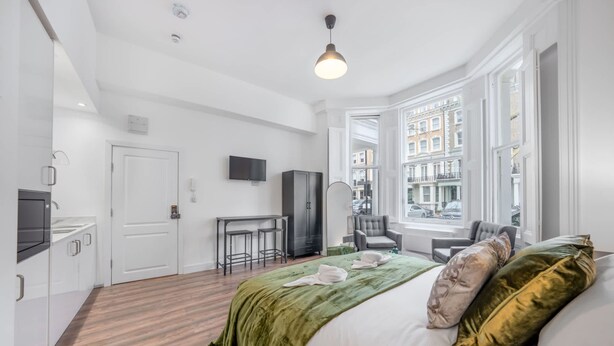 A hotel room with a bed, a desk, a chair, a TV, and a window with a city view. - Deluxe Ground Floor Studio in Knightsbridge (London)