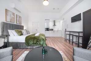 A modern hotel room with a bed, a desk, a chair, a kitchen area, and a TV mounted on the wall. - Deluxe Ground Floor Studio in Knightsbridge (London)
